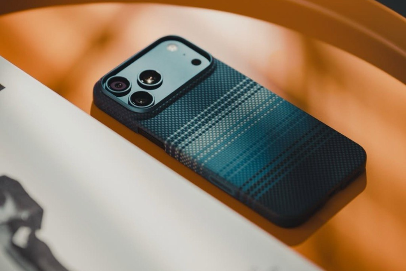 Iphone 17 Pro Max у преміальному синьому арамідному чохлі Pitaka Moonrise, що лежить на помаранчевому тлі.
